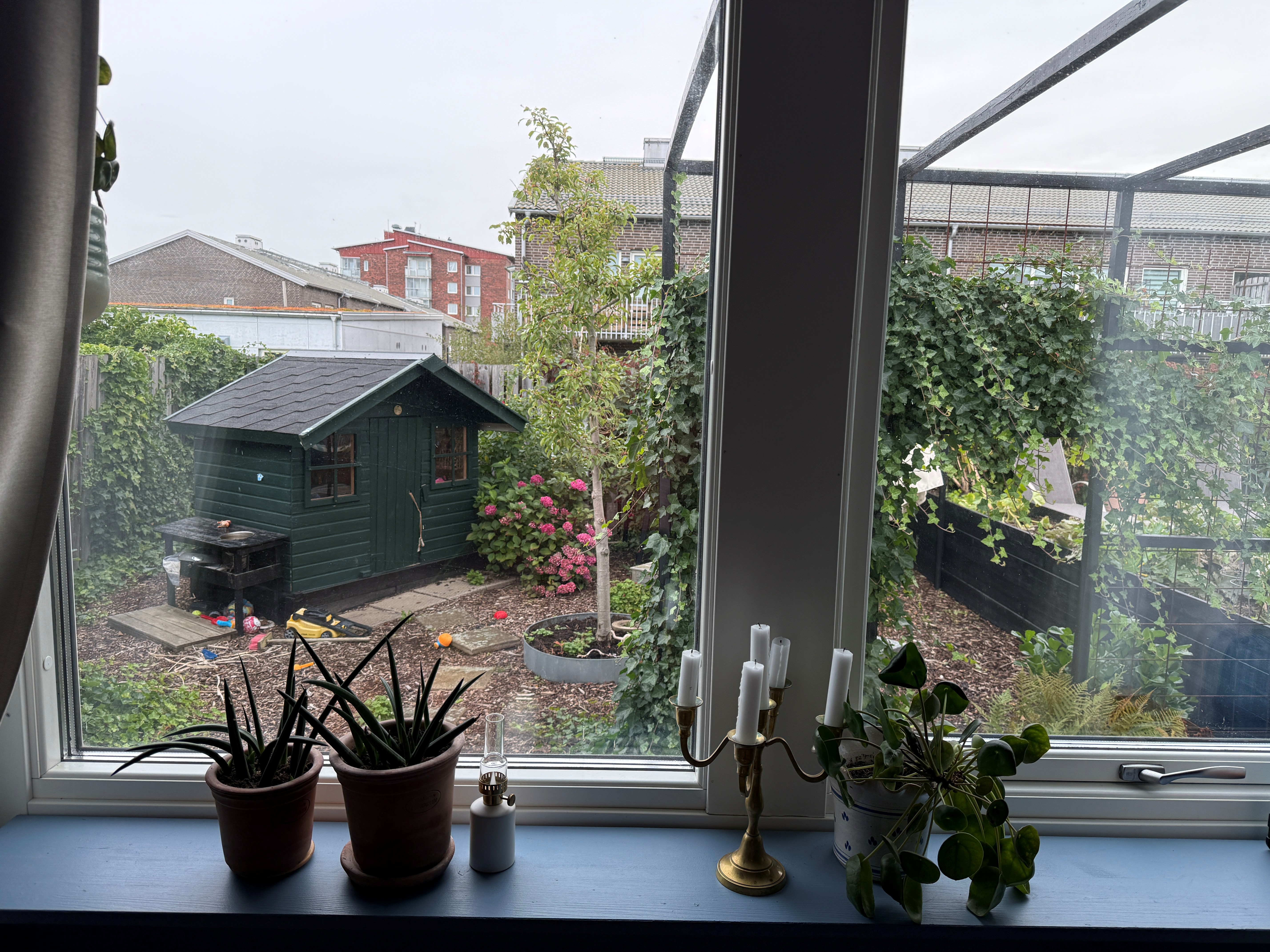Bakgården före omgestaltning, sedd från huset: grön bod, leksaker och en spaljé med klätterväxter på den lilla ytan.